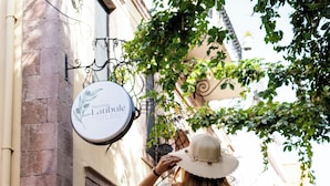 A person in a white dress standing on a cobblestone street, holding a suitcase, with a building and a sign that reads 'Macaron Latibule' in the background. - Latibule Macaron Guest House (Ayvalik)