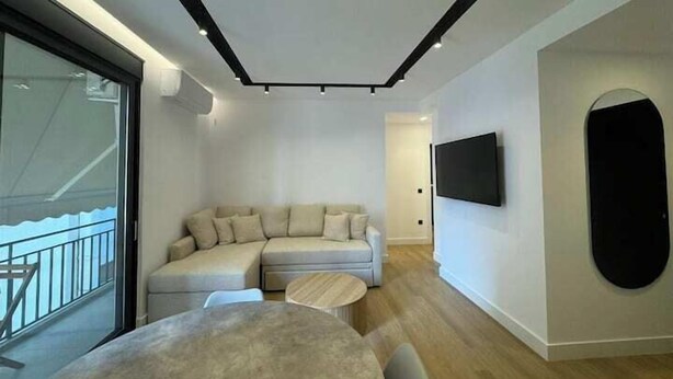 Un salon moderne avec un canapé d’angle, une table basse ronde et un téléviseur à écran plat fixé au mur.