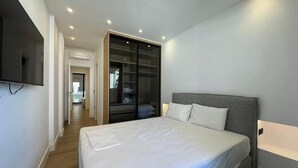 Une chambre à coucher moderne avec un grand lit, un dressing et un téléviseur fixé au mur.