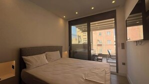 Une chambre avec un lit, une porte-fenêtre coulissante donnant sur un balcon et un téléviseur fixé au mur.