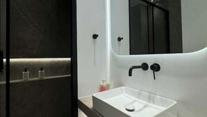 Une salle de bain moderne avec un grand miroir, un lavabo blanc et un espace douche.