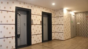 Ein Flur mit drei Aufzugtüren, strukturierten Tapeten und Holzboden.
