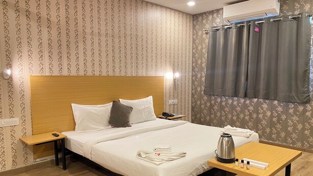 Ein Hotelzimmer mit einem Bett mit massivem Holz-Kopfteil, einem Nachttisch mit Telefon, einem Tisch mit Wasserkocher und Pflegeprodukten und einem Fenster mit Vorhängen.