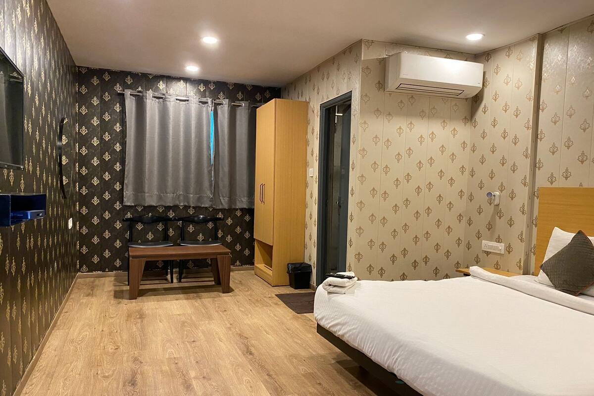 A hotel room with a bed, a bench, a wardrobe, and an air conditioning unit.