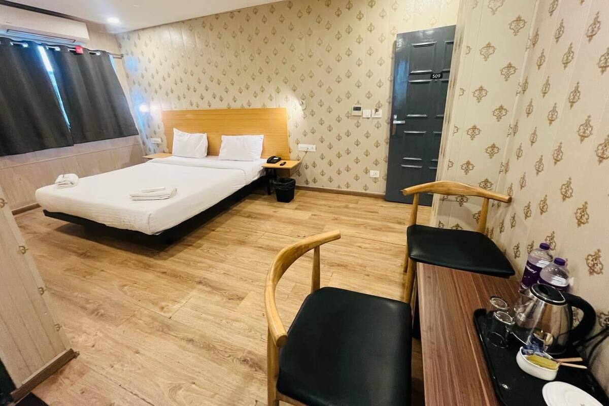 A hotel room with a bed, a desk with chairs, a wardrobe, and a small table with a kettle and cups.