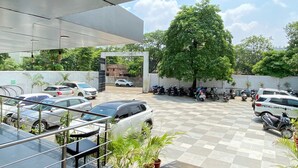 Ein Parkplatz mit Autos und Rollern, ein großer Baum und Kübelpflanzen.