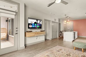 Una sala de estar moderna con un televisor de pantalla plana montado en la pared, una mesa consola de madera, un tapete estampado y un ventilador de techo.