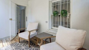 A room with a white wall, a window with a metal grid, a white chair, a wooden table, and a patterned rug. - The Magnolia on Bull, Modern | Charming | Central (Savannah)