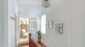 A hallway with a wooden floor, a white door, a wooden chair, and a potted plant. - The Magnolia on Bull, Modern | Charming | Central (Savannah)