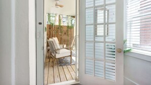 A room with a wooden floor, a white door with frosted glass panels, and a view of an outdoor area with a wooden fence and chairs. - The Magnolia on Bull, Modern | Charming | Central (Savannah)