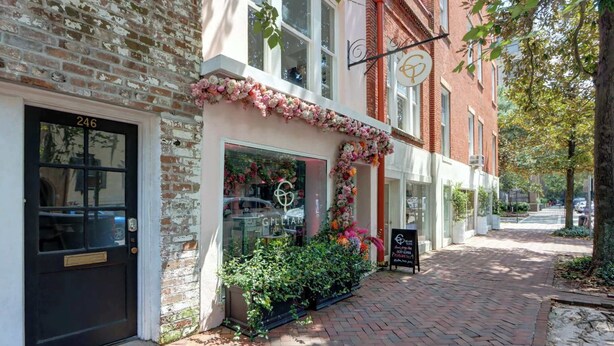 A brick building with a storefront, a black door with a number, and a signboard. - The Magnolia on Bull, Modern | Charming | Central (Savannah)