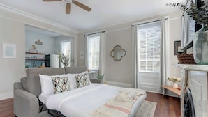 A bedroom with a bed, a sofa, a ceiling fan, a fireplace, and a window with blinds. - Suite Liberty, Elegant | Refined | Chippewa Square (Savannah)