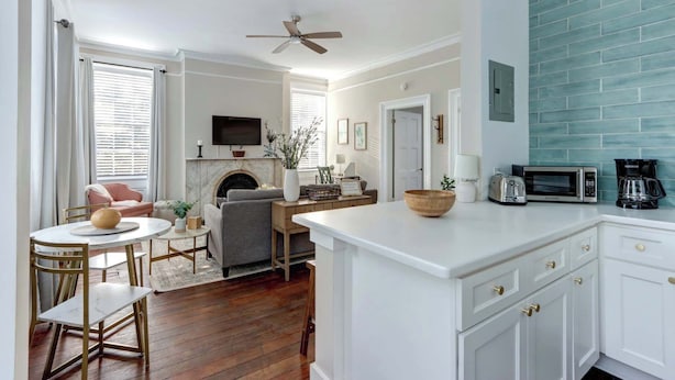 A modern kitchen with white cabinetry, a central island, and a dining area with a round table and chairs. - Suite Liberty, Elegant | Refined | Chippewa Square (Savannah)