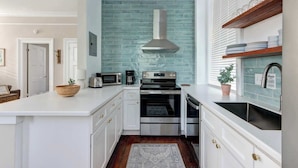 A modern kitchen with white cabinetry, a teal backsplash, stainless steel appliances, and a wooden countertop. - Suite Liberty, Elegant | Refined | Chippewa Square (Savannah)