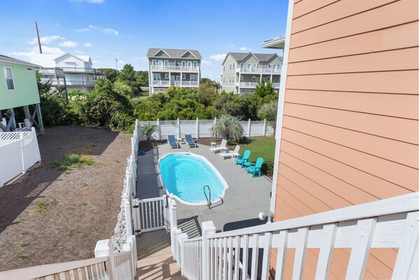A residential backyard with a swimming pool, deck chairs, and a wooden fence. - Spacious 5 BR Cottage with Private Pool, Hot Tub, Game Room & Oceanviews (Emerald Isle)