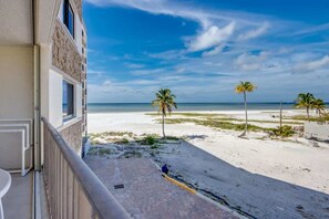 Une propriété située en bord de mer, dotée d’un balcon offrant une vue sur la plage, les palmiers et un ciel dégagé.