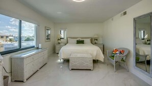 A bedroom with a large bed, a window, a radiator, a chair, and a mirror.