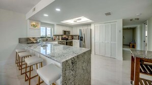 A modern kitchen with a central island, bar stools, and a view of the adjacent dining area.