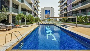 A modern hotel pool with a clear blue pool surface, surrounded by lounge chairs and a glass balustrade.