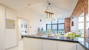 A modern kitchen with a central island, a hanging light fixture, and a view of the city through large windows.