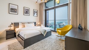 A modern hotel room with a large bed, a desk, a chair, and a balcony with a view.