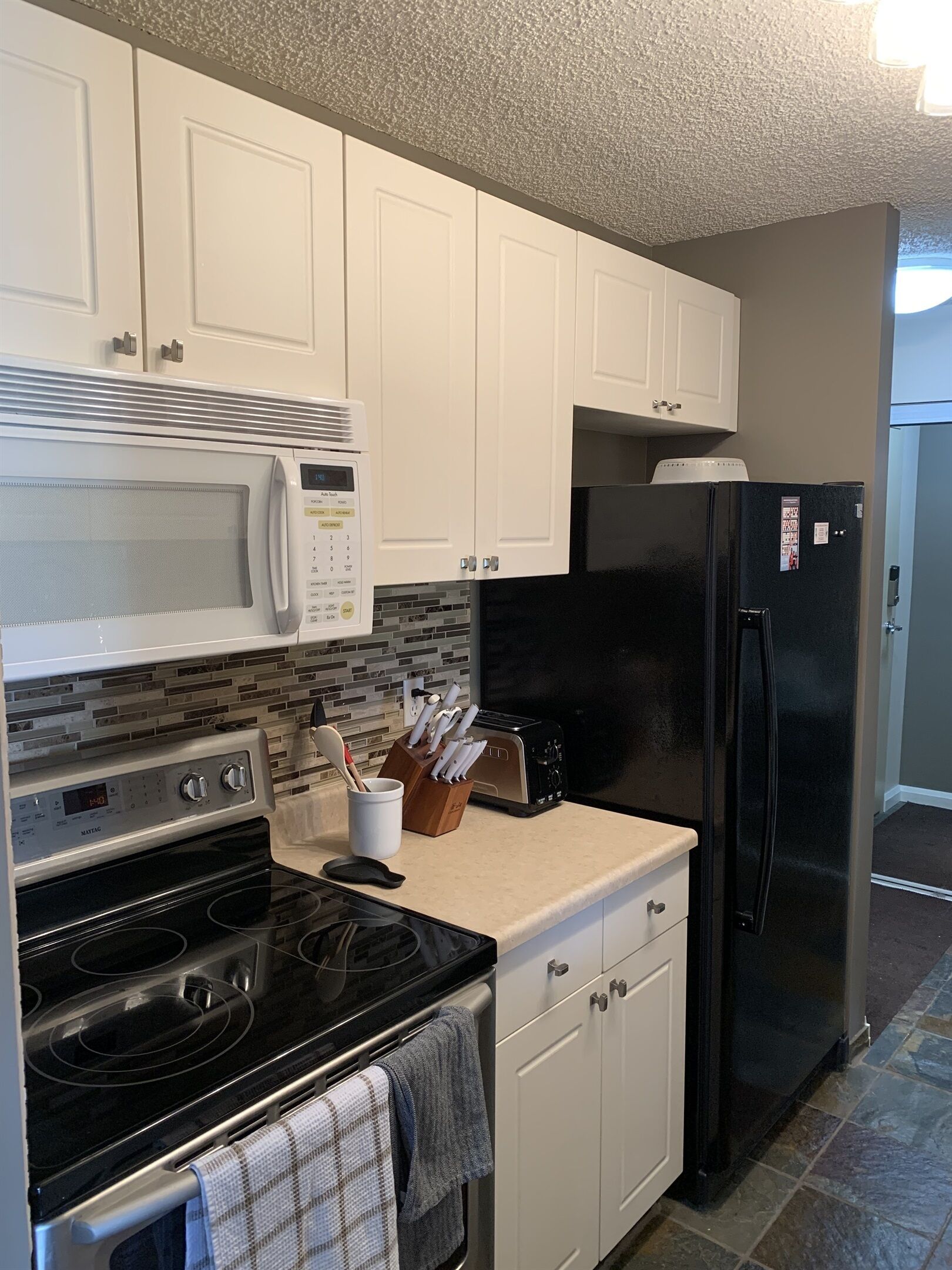 A kitchen with white cabinets, a black refrigerator, a microwave, a toaster, and a stove.
