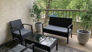 A balcony with wicker furniture, including a chair, sofa, and table, and two potted plants. - Cozy Condo close to LRT, Stadium and Expo Center. (EDMONTON)
