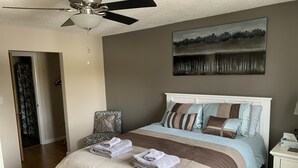 A bedroom with a bed, a chair, a ceiling fan, a painting, and a nightstand. - Cozy Condo close to LRT, Stadium and Expo Center. (EDMONTON)
