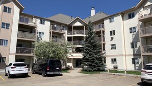 A multi-story apartment building with balconies and a parking area. - Cozy Condo close to LRT, Stadium and Expo Center. (EDMONTON)