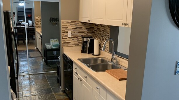 A modern kitchen with white cabinets, a stainless steel sink, and a tiled backsplash. - Cozy Condo close to LRT, Stadium and Expo Center. (EDMONTON)