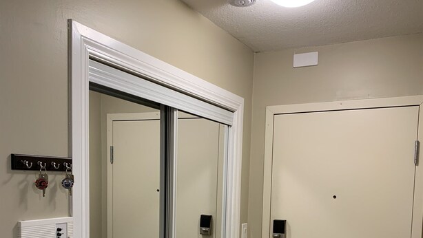 A room with a sliding door, a coat rack with keys, a smoke detector, and a thermostat on the wall. - Cozy condo, close to Northgate mall and Ring road Top Floor. (REGINA)