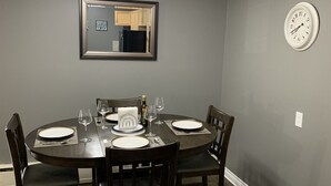 A dining room with a round table set for four, equipped with plates, glasses, and cutlery. A mirror hangs on the wall above the table, and a clock is visible to the right. - Cozy condo, close to Northgate mall and Ring road Top Floor. (REGINA)