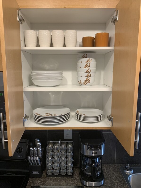Una cocina con una alacena empotrada que contiene vajilla blanca y marrón, una cafetera y un bloque de cuchillos.