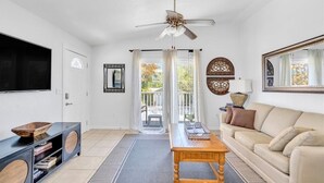 Ein Wohnzimmer mit Deckenventilator, Wand-Fernseher, Couchtisch aus Holz, beiges Sofa und einem großen Spiegel.