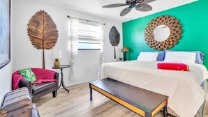 Ein Schlafzimmer mit Bett, einer Bank, einem Deckenventilator und dekorativer Wandgestaltung mit Blättern.
