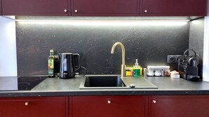 Eine Küche mit schwarzem Arbeitsplatz, einer Spüle, einer Kaffeemaschine, einer Flasche Olivenöl und einem Wasserkocher.