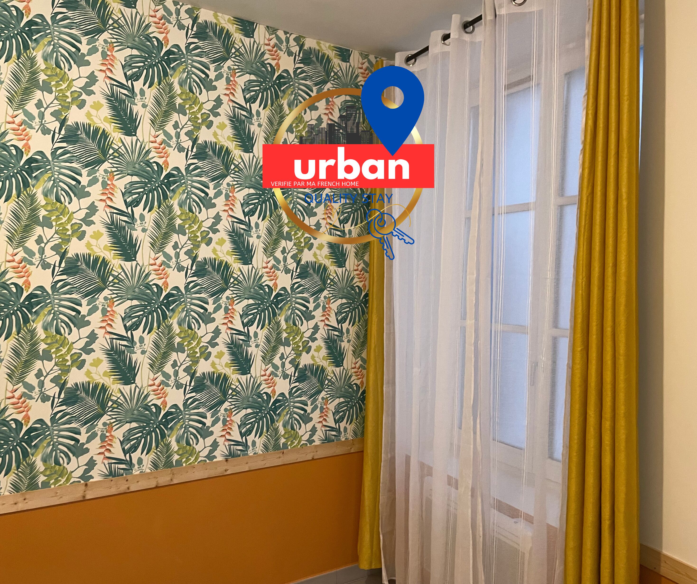 Ein Zimmer mit Wandpapier mit tropischen Blättern, einem gelben Vorhang und einem Fenster mit weißen Vorhängen.