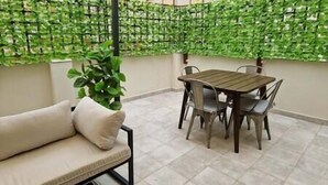 A balcony with a wooden table and chairs, a beige sofa, and a green leafy wall.