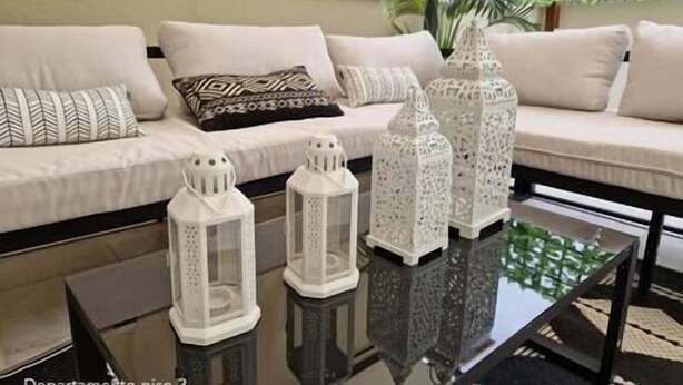 A modern living room with a sofa, cushions, and three white lanterns on a glass coffee table.