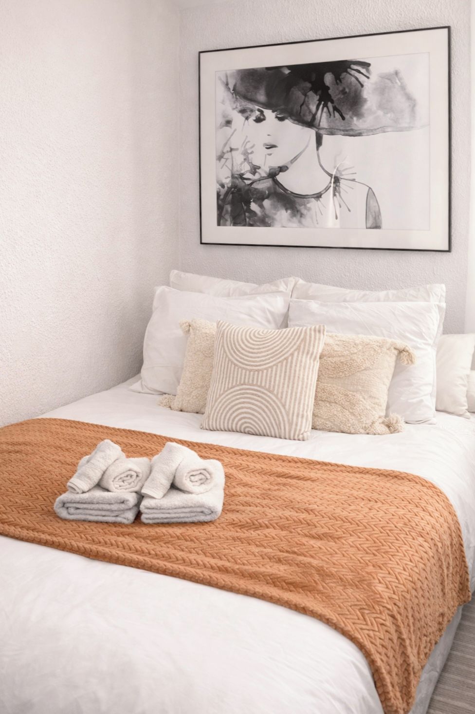 A neatly made bed with a brown blanket, white pillows, and a folded towel on the bed.