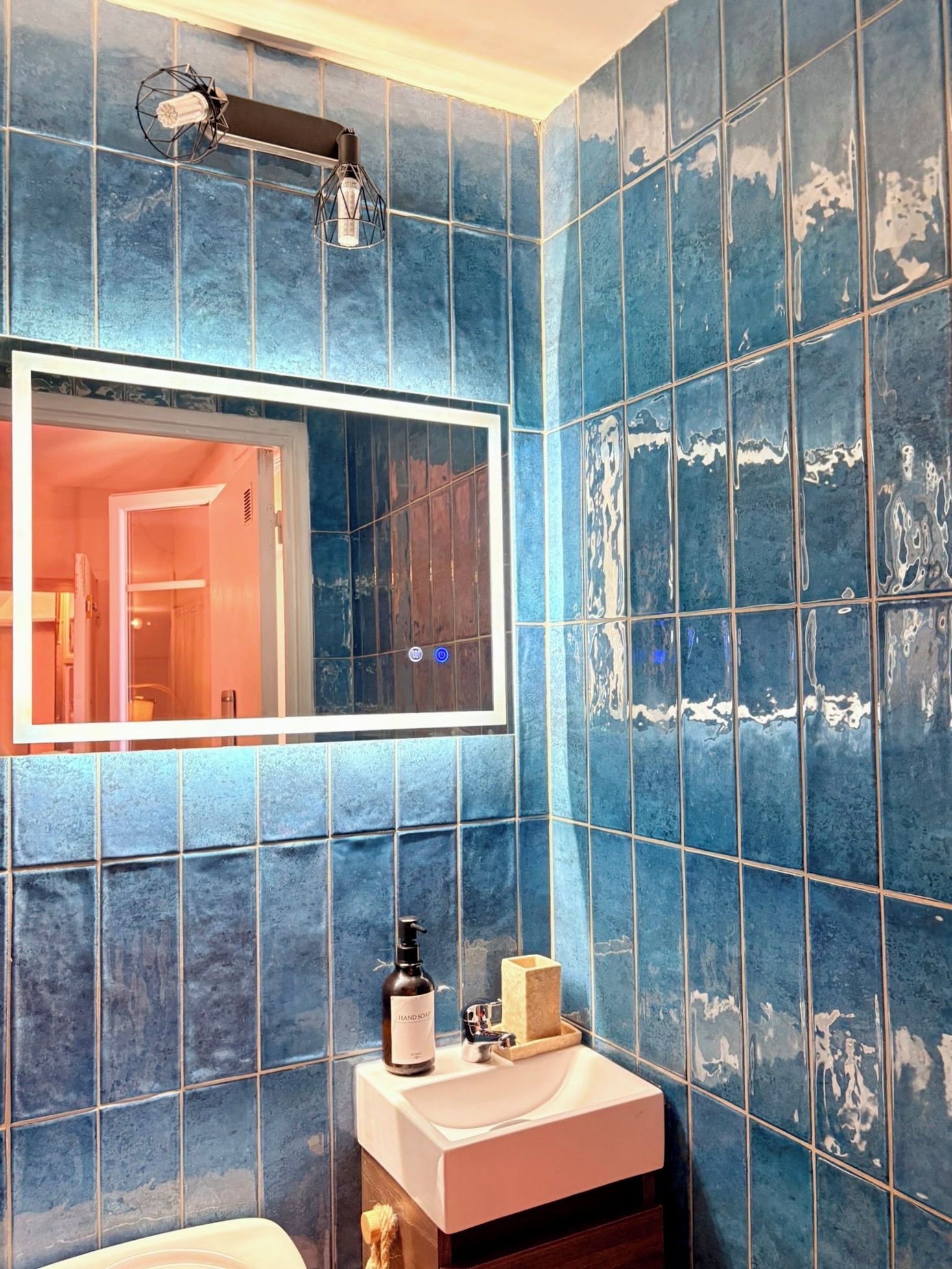 A bathroom with blue tiles, a white sink, a mirror, and a handheld showerhead.