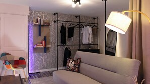 A modern living room with a sofa, a chair, a bookshelf, and a clothing rack. - Hyper-centre de Perpignan : Studio chic à deux pas de tout ! (Perpignan)