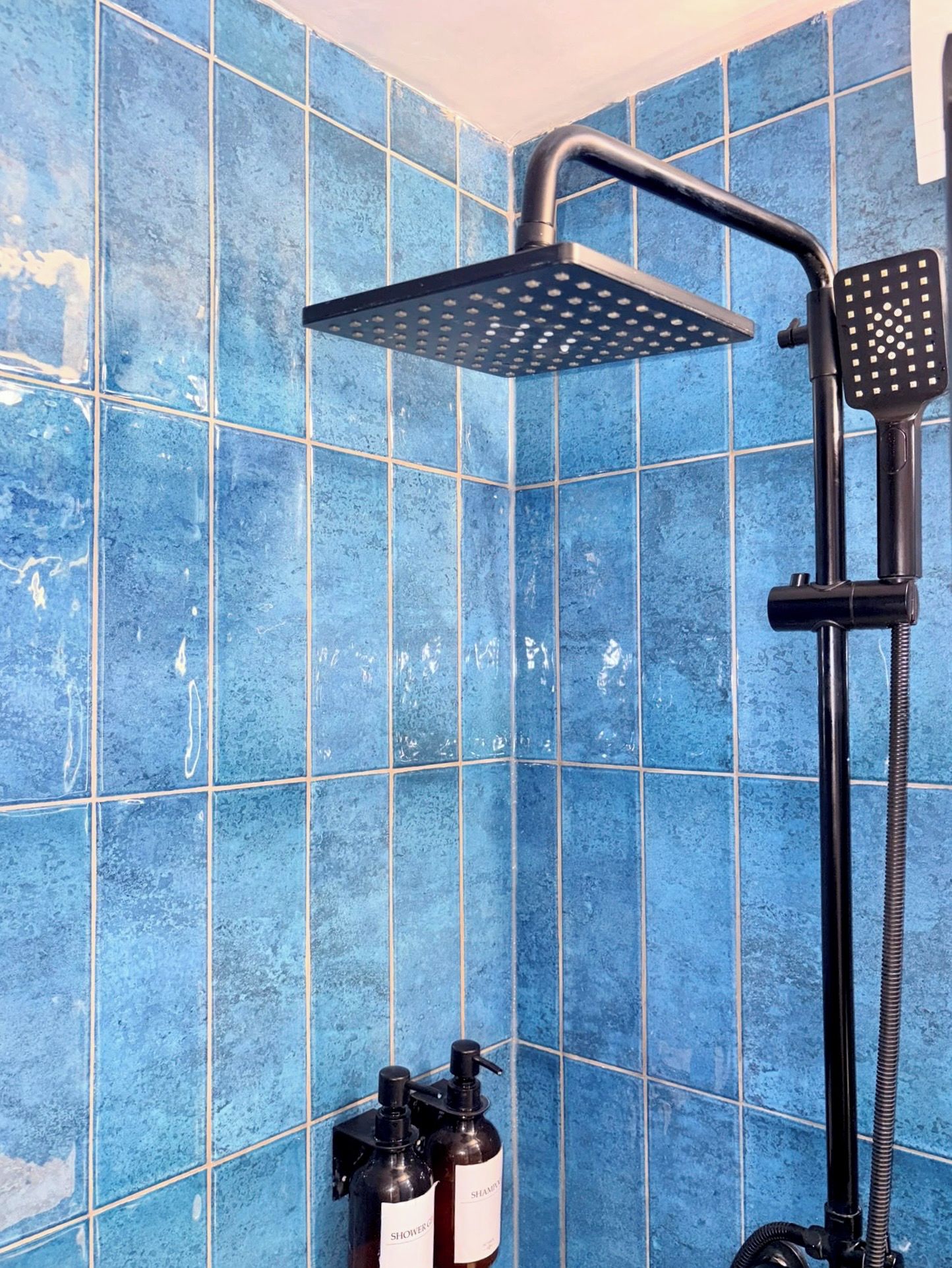 Een douche met een handdouche en een vaste douchekop, beide bevestigd aan een muur met blauwe tegels.