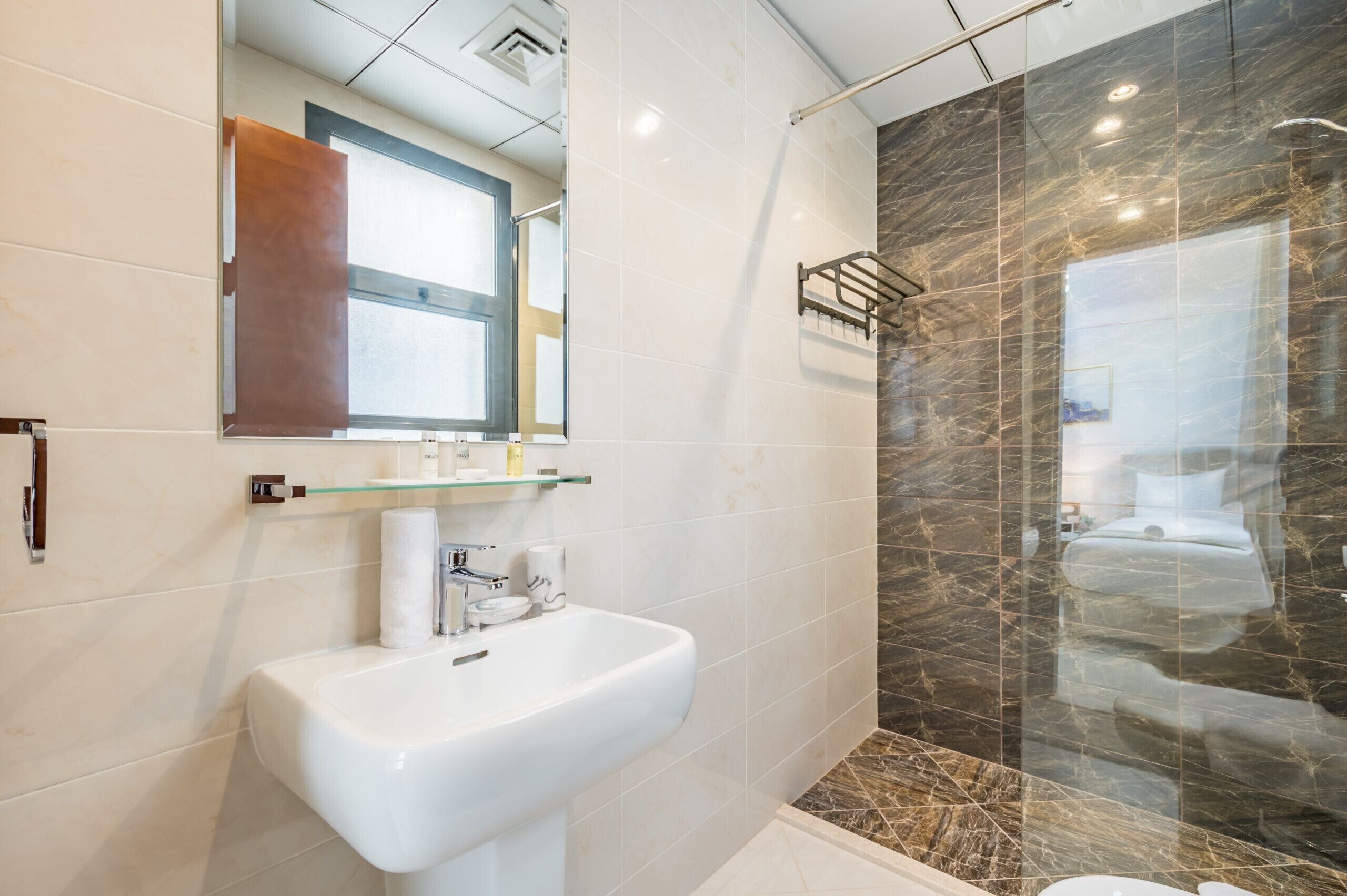 Un baño moderno con lavamanos blanco, cabina de ducha de vidrio y pared de ducha con azulejos de mármol.