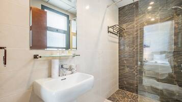 Un baño moderno con lavamanos blanco, cabina de ducha de vidrio y pared de ducha con azulejos de mármol.