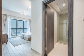 Ein modernes Hotelzimmer mit großem Fenster, einem Bett, einem begehbaren Kleiderschrank und einer Duschkabine.