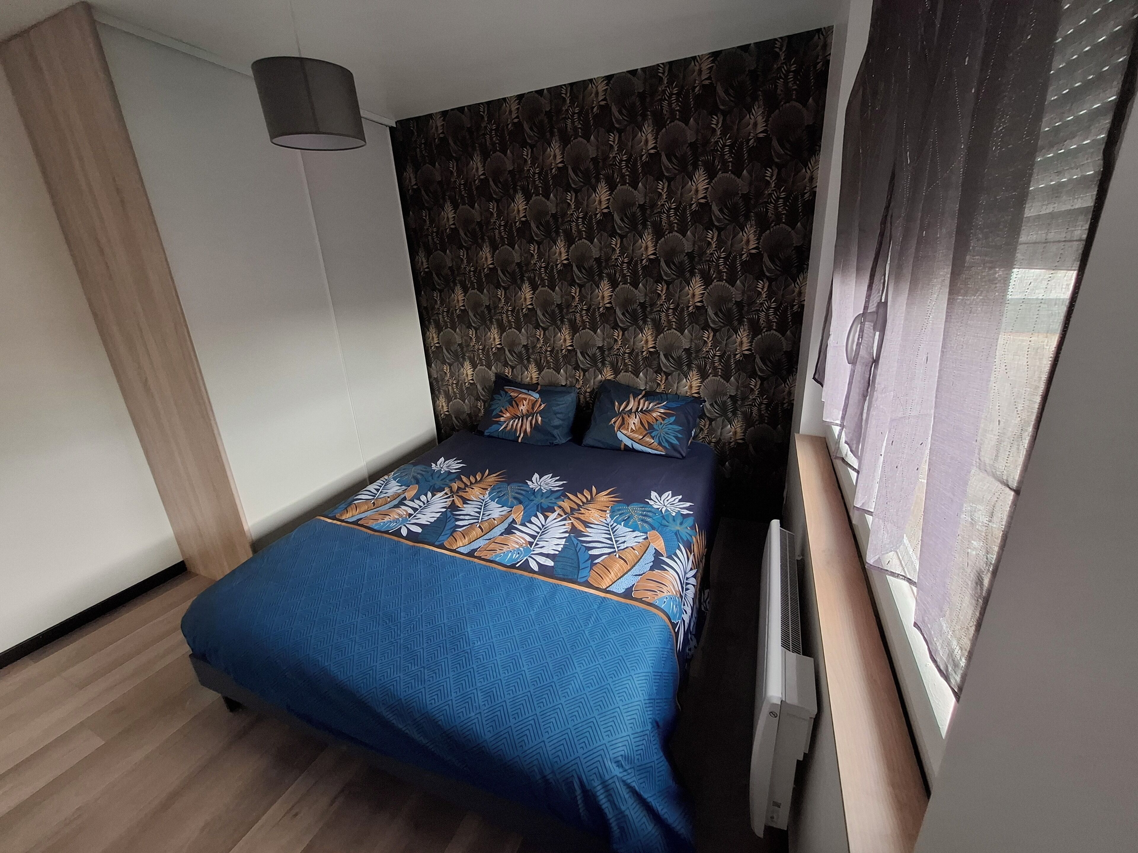 Ein Schlafzimmer mit einem gemusterten Kopfteil, einem Bett mit blauer Bettdecke und einem Fenster mit Jalousien.