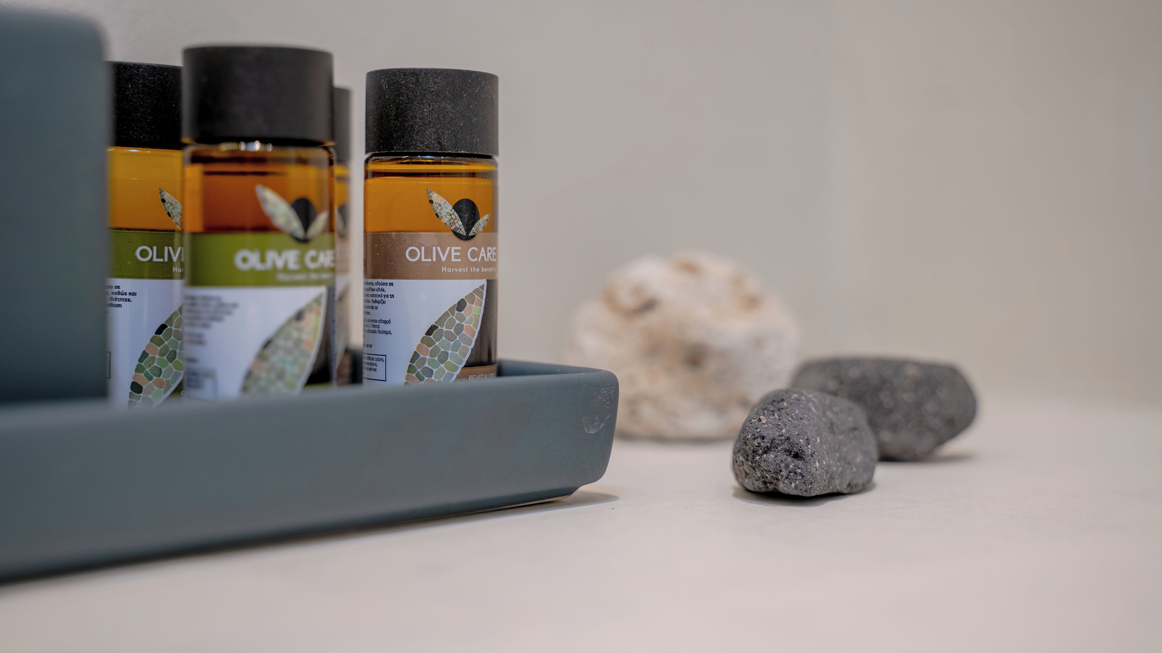 Tres botellas de productos de cuidado con aceite de oliva en un recipiente gris con superficie texturizada.