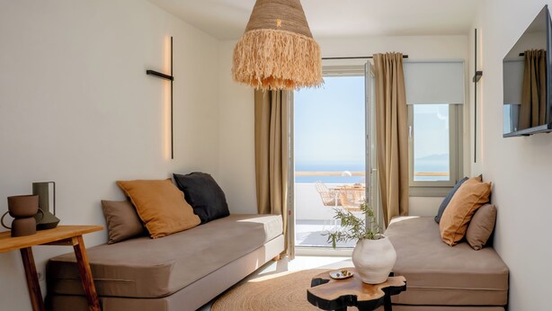 A modern living room with a sofa, a coffee table, and a hanging light fixture. - Ico Santorini (Santorini)