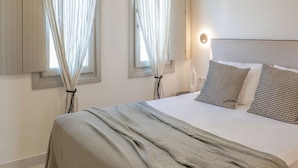 A bedroom with a large bed, a hanging light fixture, and curtains on the windows. - Ico Santorini (Santorini)